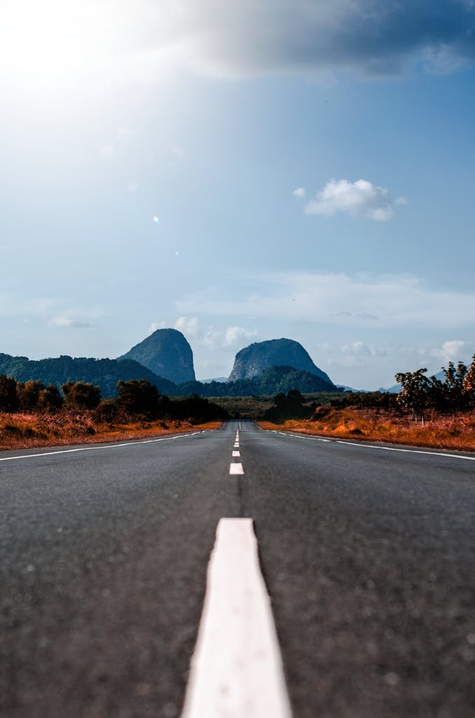 Long straight road leading to distant mountains under a bright blue sky.